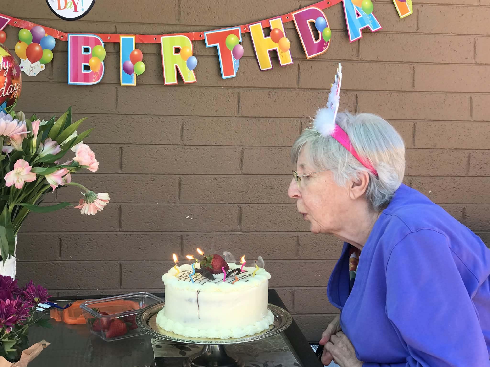 Resident blowing out candles on a birthday cake beneath a birthday banner