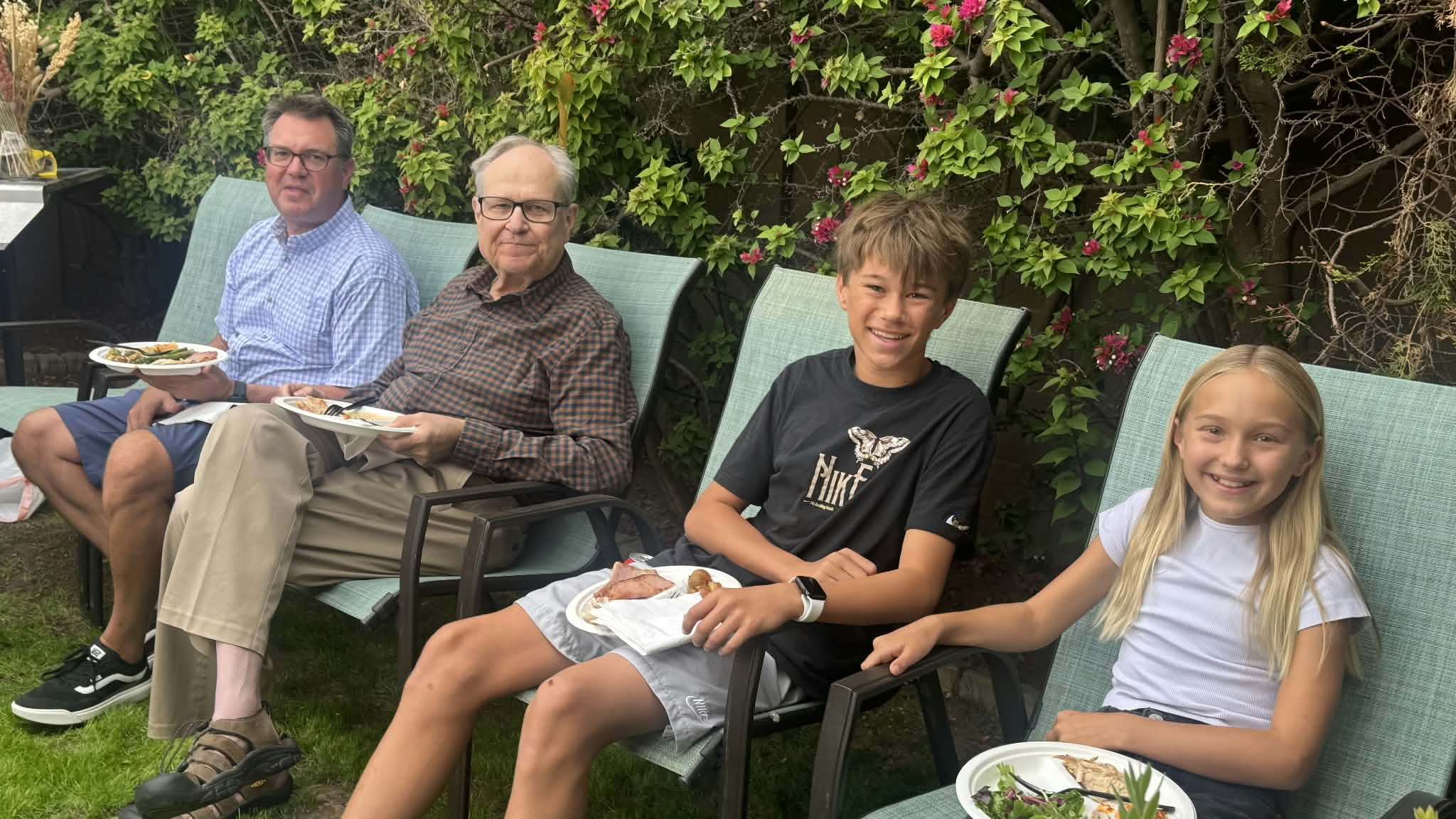 Two older guests and two children sitting together outdoors with plates of food