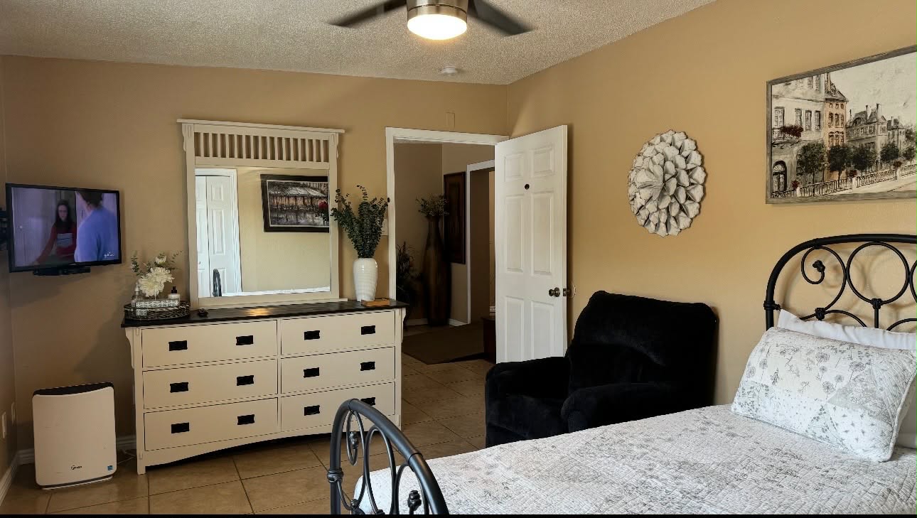 Bedroom showing a dresser, mirror, television, bed and recliner