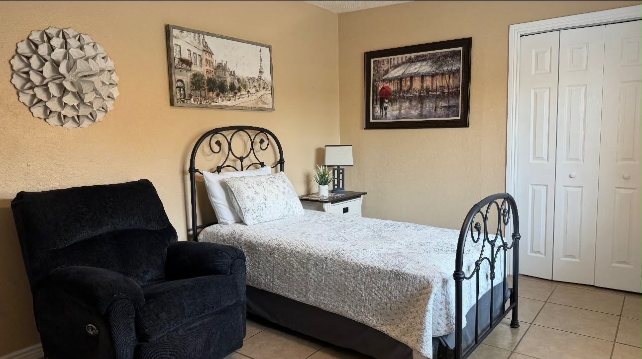 Bedroom with an iron bed, bedside table, artwork and a dark recliner