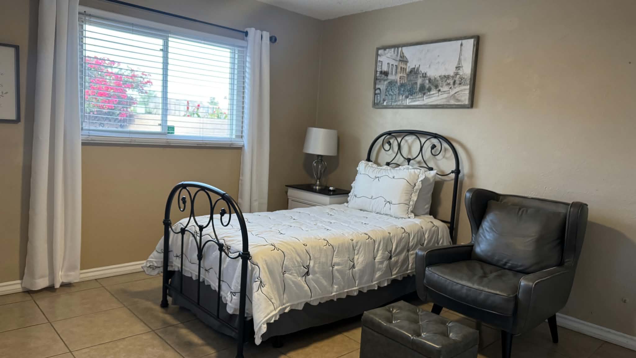 Bedroom with a window, iron bed, armchair and footstool